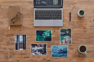 Laptop und ausgedruckte Fotos auf einem Holzschreibtisch von oben, Symbolbild für Alt-Texte bei Bildern