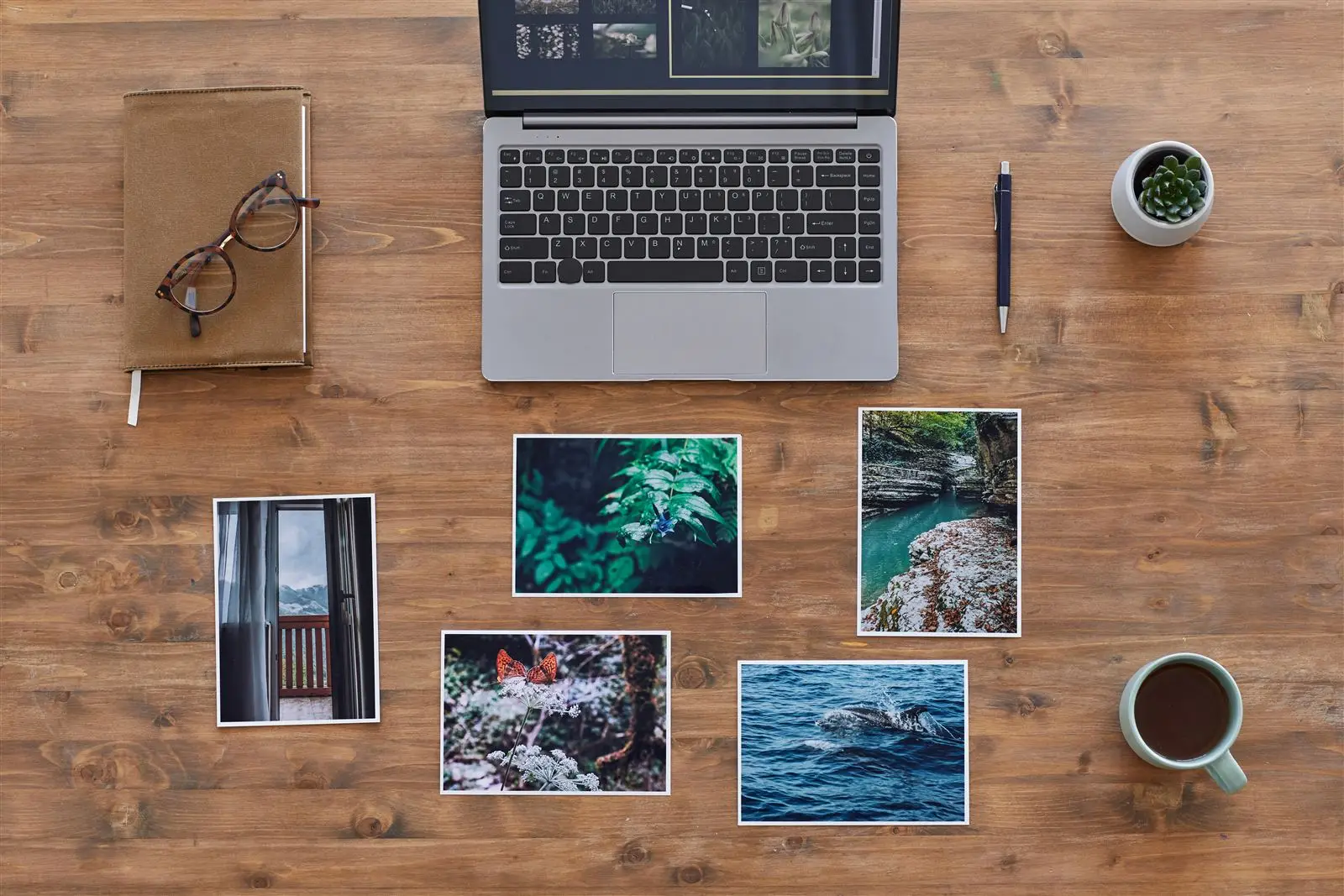 Laptop und ausgedruckte Fotos auf einem Holzschreibtisch von oben, Symbolbild für Alt-Texte bei Bildern