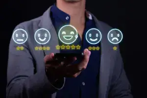 Mann h&auml;lt ein Smartphone, dar&uuml;ber schweben Smileys mit einem bis f&uuml;nf Sternen, Symbolbild f&uuml;r Google-Bewertungen
