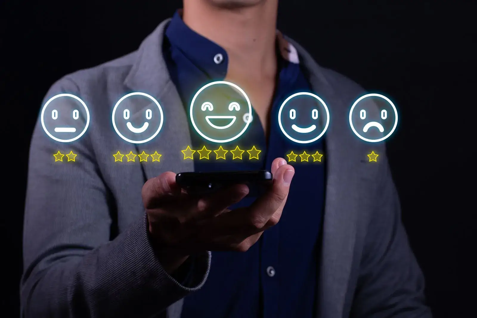 Mann hält ein Smartphone, darüber schweben Smileys mit einem bis fünf Sternen, Symbolbild für Google-Bewertungen