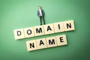 Buchstabensteine bilden die Wörter Domain Name, darüber steht eine kleine Figur im Anzug, Symbolbild für die eigene Domain