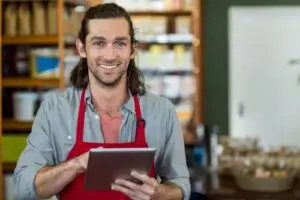 Ladenbesitzer mit Tablet hinter der Theke – Symbolbild für die Frage nach der eigenen Website