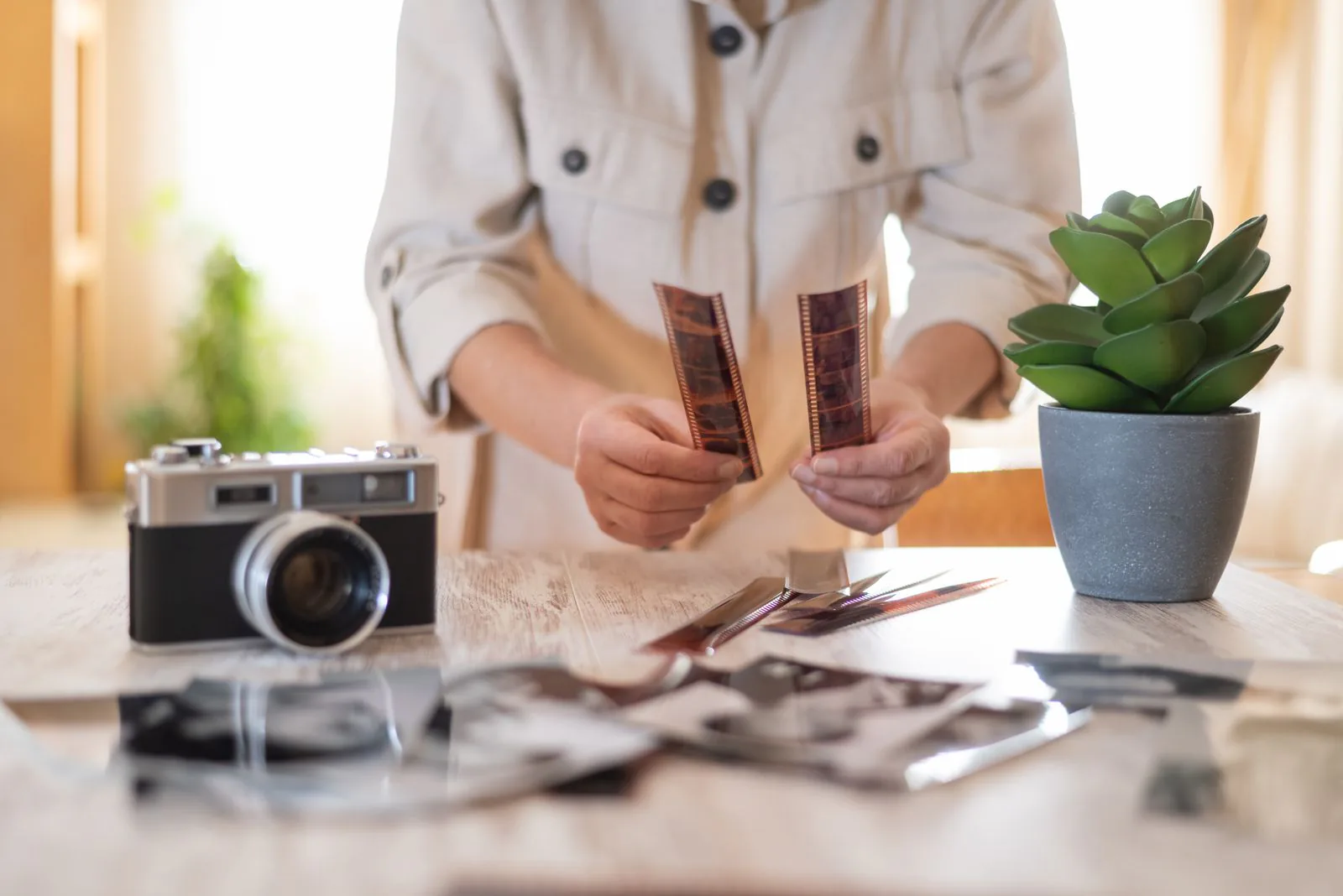 Hände halten Filmnegative über einem Tisch mit Kamera und Schwarzweißfotos, Symbolbild für Bildrechte auf der Website
