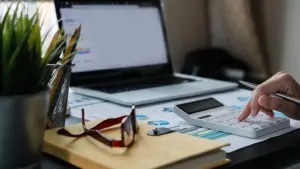 Hände mit Taschenrechner neben Laptop und Diagrammen, Symbolbild für das Google-Ads-Budget