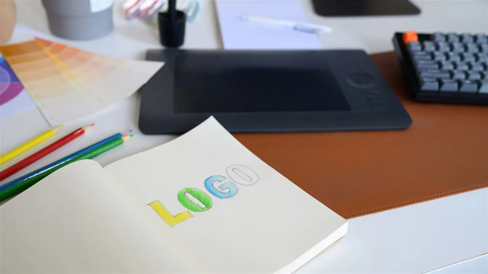 Logo-Skizze mit Farbstiften und Tablet auf dem Schreibtisch eines Designers – Symbolbild für Logo-Redesign