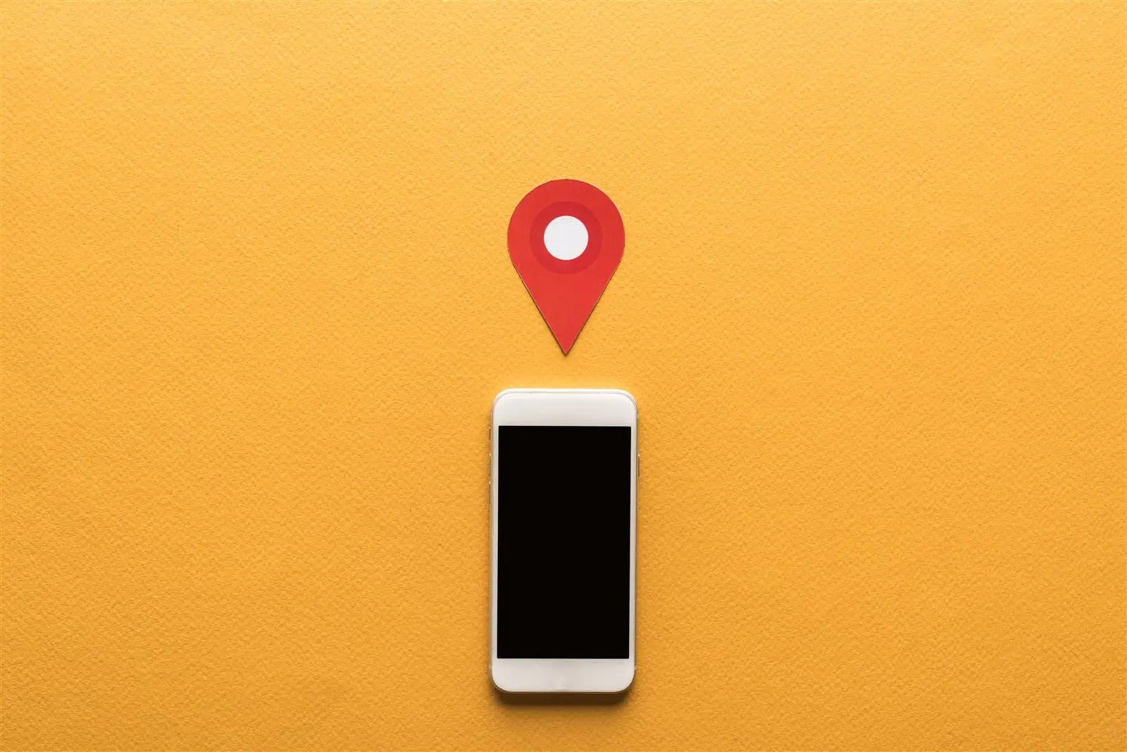 Smartphone mit Standortmarkierung auf orangefarbenem Hintergrund – Symbolbild für Beiträge im Google-Unternehmensprofil