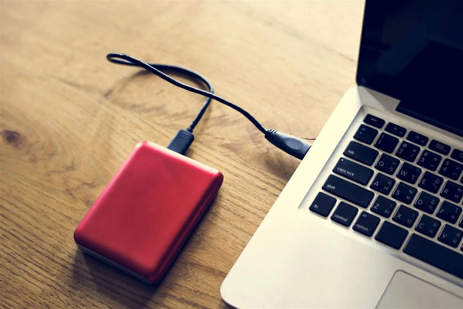 Rote externe Festplatte per Kabel mit einem Laptop auf einem Holztisch verbunden, Symbolbild für ein Website-Backup