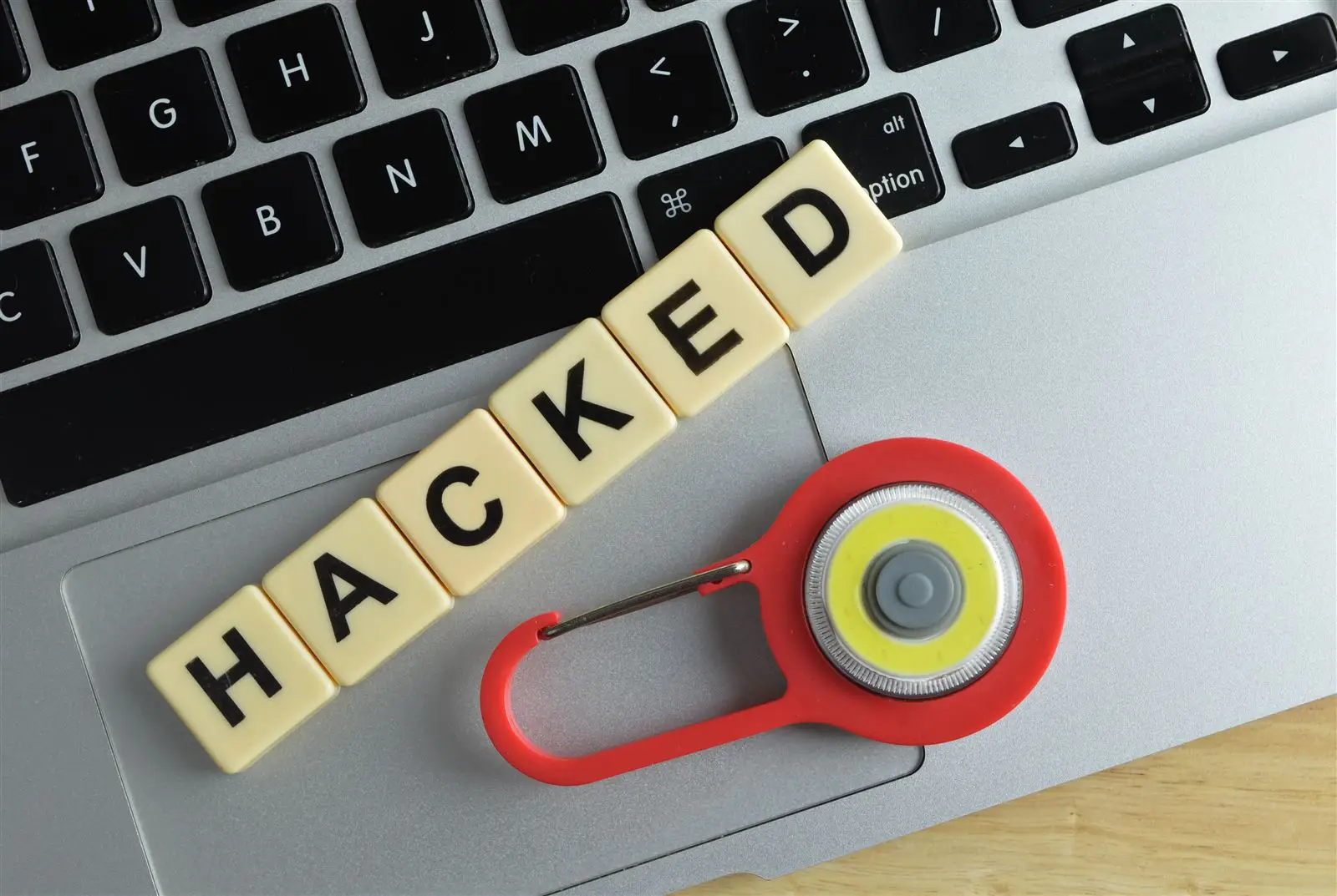 Vorhängeschloss, Laptop und Buchstabensteine mit dem Wort HACKED – Symbolbild für eine gehackte Website