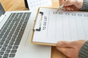 Person hakt Punkte auf einer Checkliste neben einem Laptop ab – Symbolbild für Website-Wartung als Abo