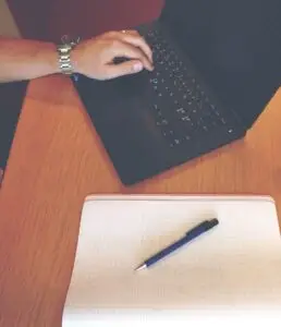 Geschäftsmann arbeitet am Laptop, daneben ein Notizblock – Symbolbild für die Textmenge einer Website